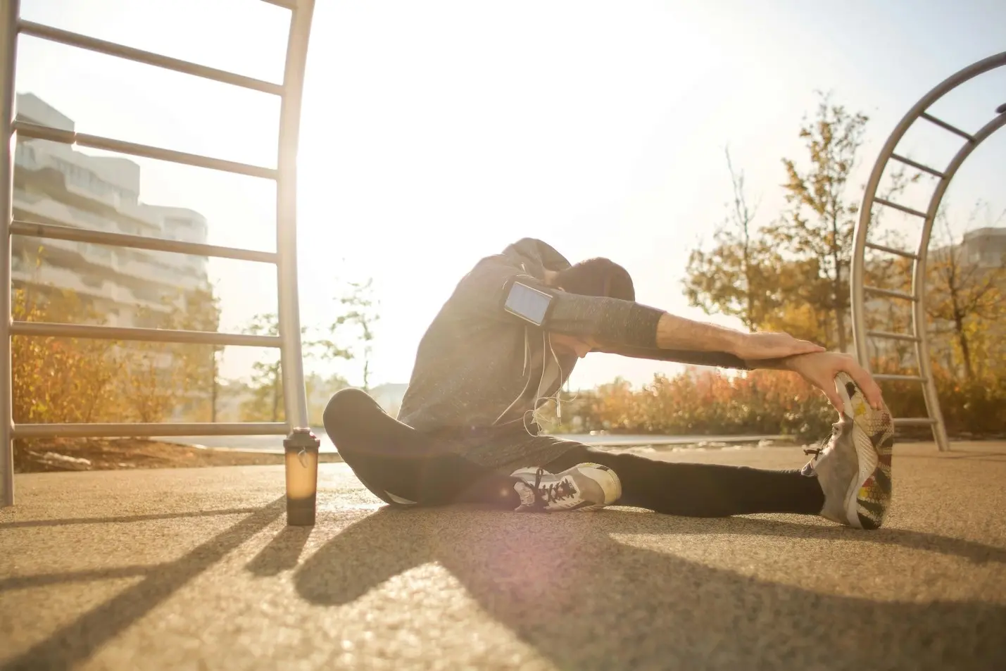 Athlete stretching outdoors before workout with water bottle and fitness gear, promoting healthy lifestyle, flexibility, and sports recovery.