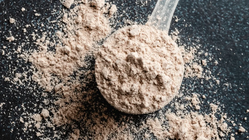 Scoop of whey protein powder on a dark surface, ideal for fitness, muscle recovery, and sports nutrition supplements.