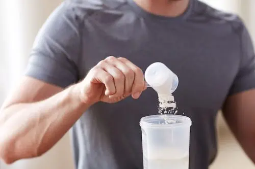 Man in sportswear pouring whey protein powder into a shaker bottle, preparing a protein shake for fitness, muscle recovery, and workout nutrition.