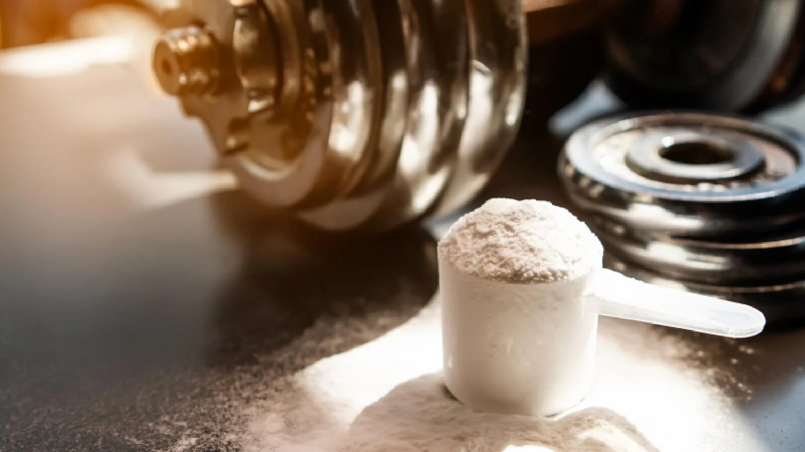Scoop of whey protein powder placed on gym floor with dumbbells in the background, representing strength training, muscle growth, and fitness nutrition.