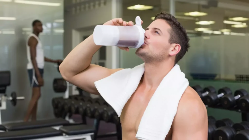 Fit man drinking whey protein shake at the gym after workout, promoting muscle recovery, strength training, and sports nutrition.