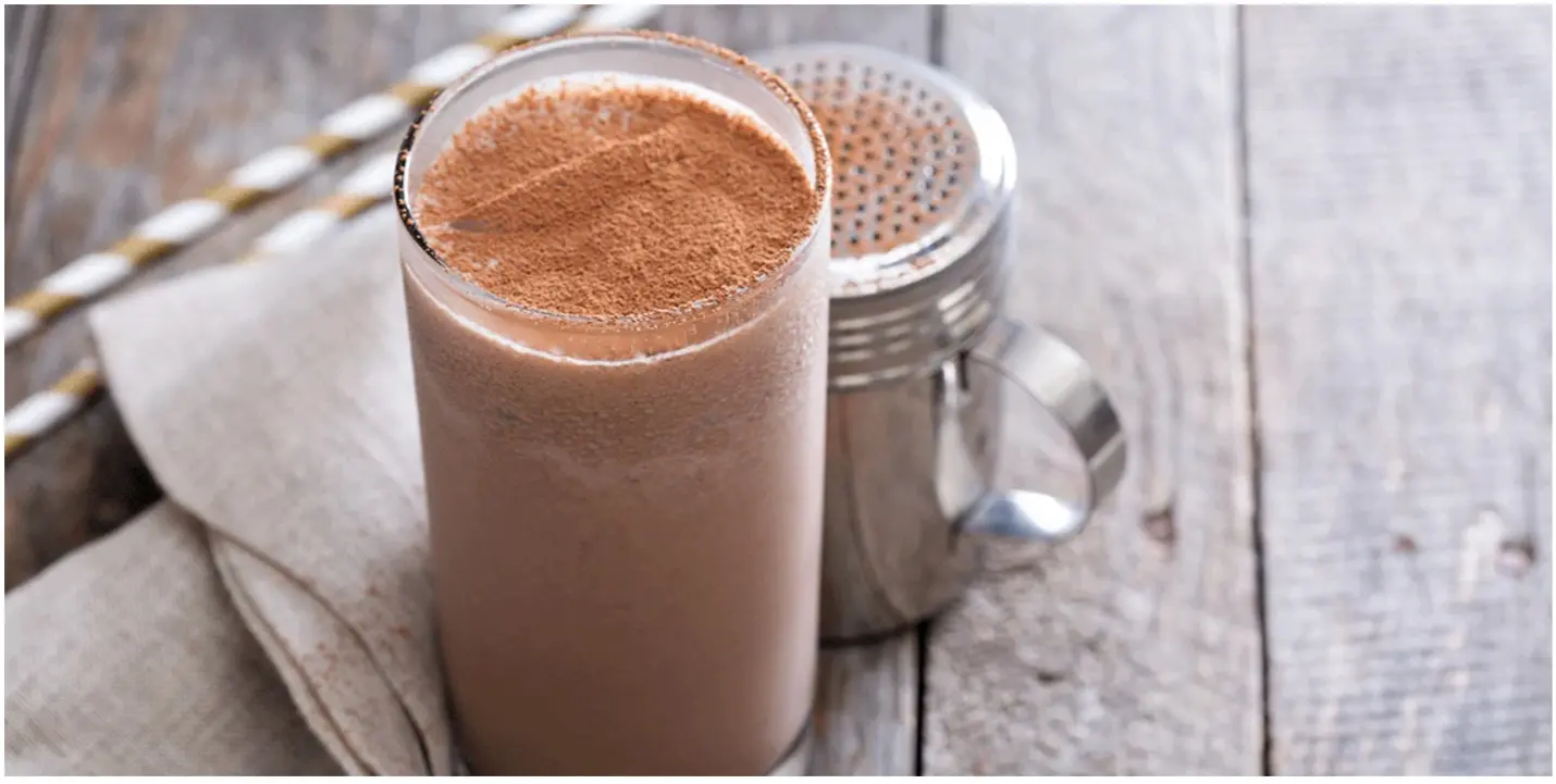 Glass of chocolate whey protein shake on rustic wooden table, perfect for fitness nutrition, muscle recovery, and post-workout energy.