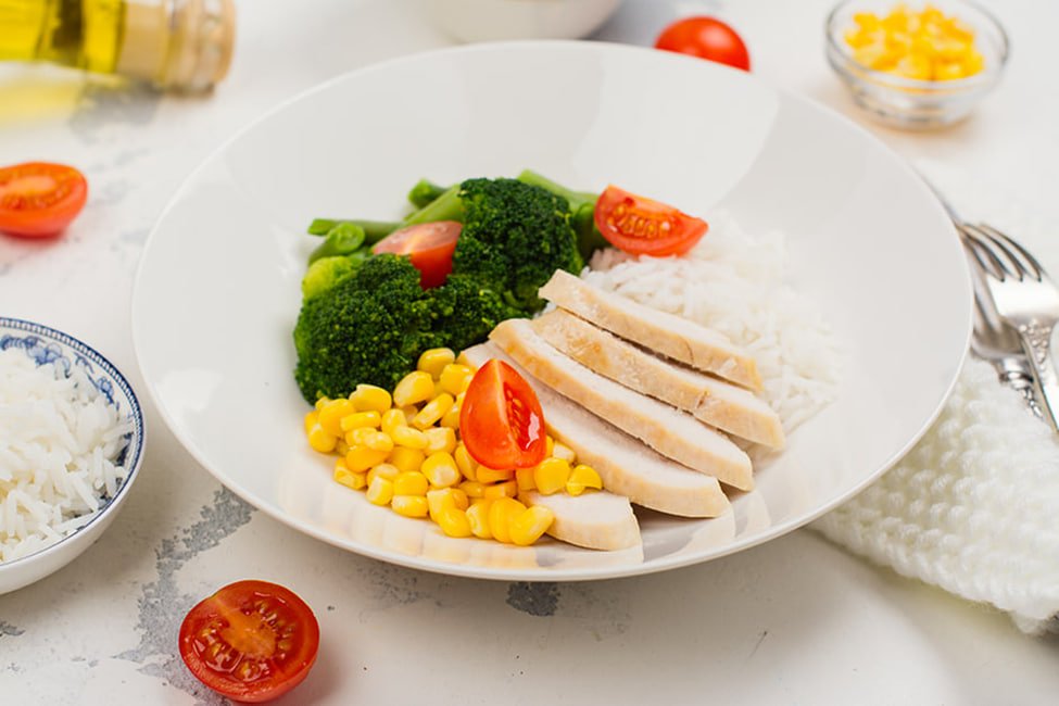Balanced chicken, rice and vegetable meal beside a glass of water and a closed supplement bottle