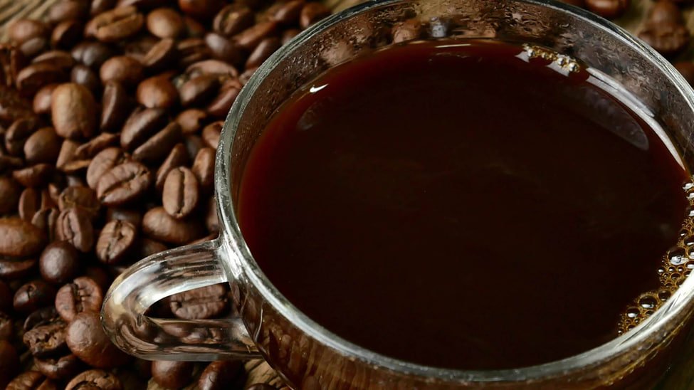 Black coffee, a glass of water and an unbranded supplement bottle on a walnut table